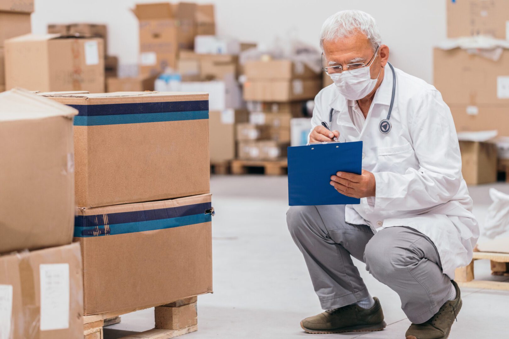 Masked worker inspecting boxes in a warehouse.