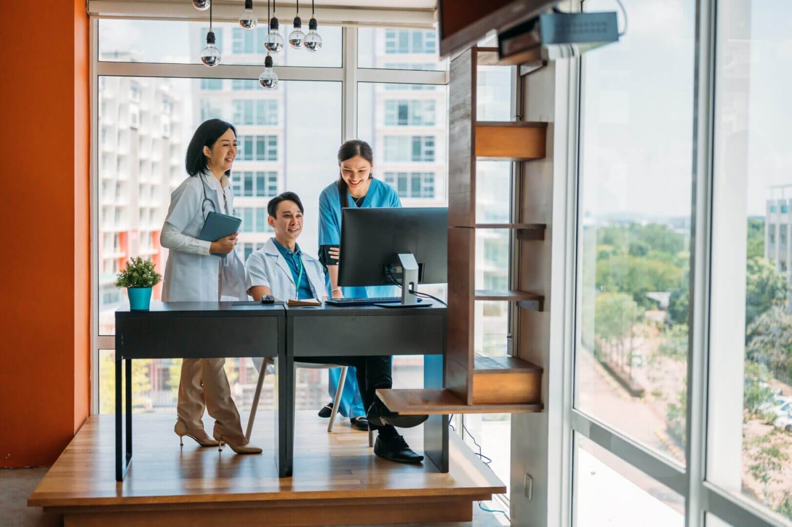 Doctors discussing at office desk by window.