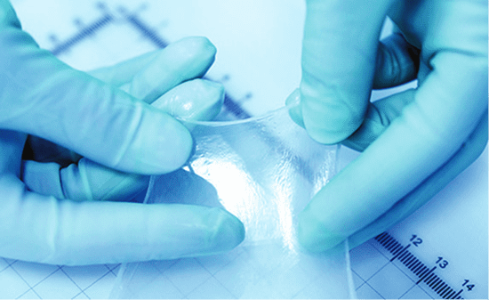 Gloved hands stretching transparent medical film.